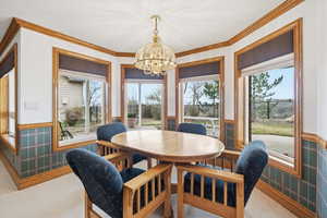 Carpeted dining space featuring wallpapered walls, a wainscoted wall, suspended lighting, and ornamental molding