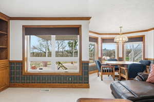 Living room featuring wainscoting, suspended lighting, wallpapered walls, light carpet, and crown molding