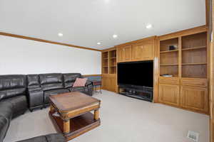 Living room with recessed lighting, crown molding, light colored carpet, and built in shelves