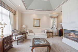Living room with crown molding, a wainscoted wall, light colored carpet, a glass covered fireplace, and lofted ceiling