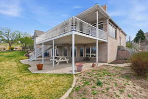 Back of property featuring a patio, brick siding, a lawn, a chimney, and a wooden deck