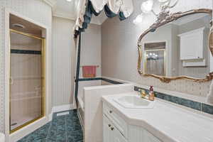 Full bath with wallpapered walls, vanity, a shower stall, ornamental molding, and dark tile patterned flooring