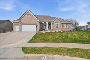 View of front of property with covered porch, a garage, brick siding, and a front lawn