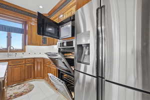 Kitchen featuring stainless steel fridge, a warming drawer, light tile patterned floors, wood finish cabinets, and crown molding