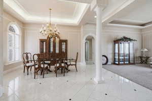 Dining room with ornate columns, a raised ceiling, healthy amount of natural light, light tile patterned flooring, and hanging lights