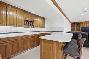 Kitchen with open floor plan, a breakfast bar, light countertops, tasteful backsplash, and wood finish cabinetry