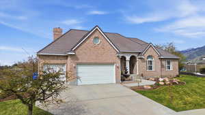 View of front of property with brick siding, concrete driveway, a front lawn, a chimney, and an attached garage