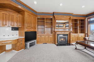 Unfurnished living room featuring built in shelves, ornamental molding, light colored carpet, a fireplace with flush hearth, and recessed lighting