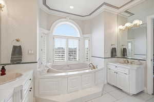 Bathroom featuring wallpapered walls, two vanities, a garden tub, crown molding, and light tile patterned floors