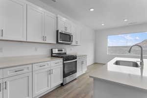 Kitchen featuring stainless steel appliances, dark wood-style flooring, white cabinetry, recessed lighting, and light stone counters