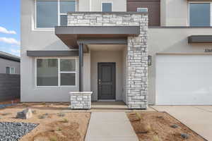 Entrance to property with stone siding, stucco siding, and a garage