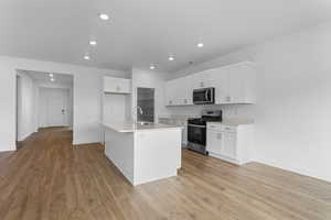 Kitchen featuring white cabinetry, stainless steel appliances, an island with sink, light wood-type flooring, and recessed lighting