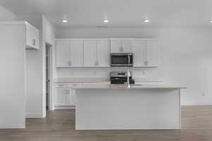 Kitchen featuring white cabinets, stainless steel appliances, an island with sink, dark wood-style floors, and recessed lighting