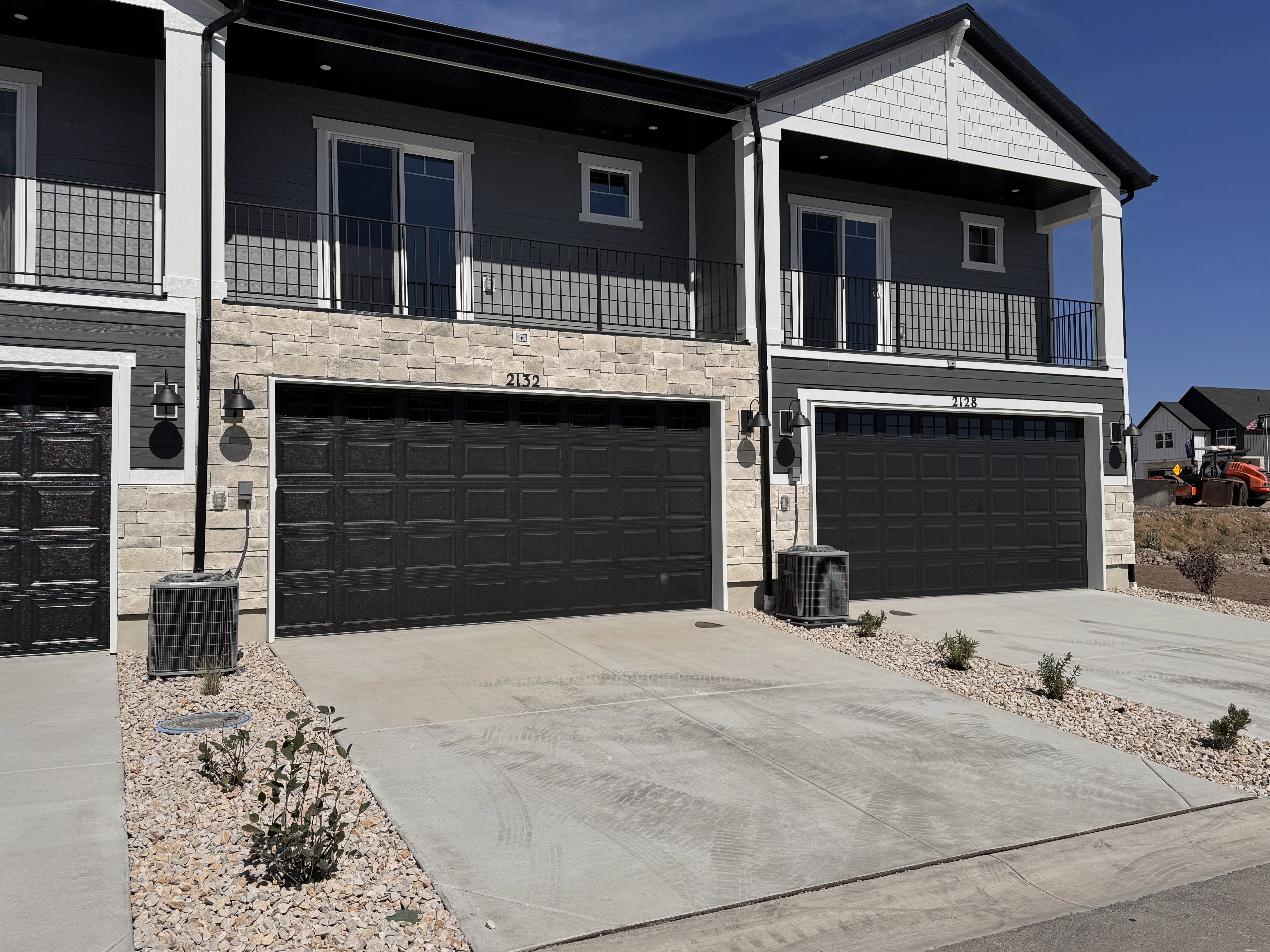 Contemporary townhome exterior featuring dark gray siding, stone veneer accents, and a prominent front-facing garage with a black door