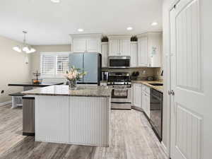 Kitchen with light stone countertops, stainless steel appliances, a kitchen island, light wood-type flooring, and white cabinets