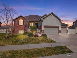 View of front of home with brick siding, a gate, an attached garage, driveway, and stucco siding