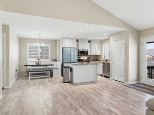 Kitchen with white cabinetry, light wood-style floors, stainless steel appliances, a center island, and lofted ceiling