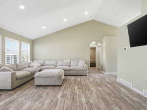 Living room with light wood-type flooring, recessed lighting, arched walkways, and a high ceiling