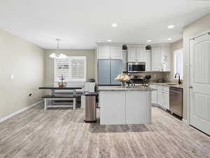 Kitchen featuring light stone counters, white cabinets, a kitchen island, light wood-type flooring, and stainless steel appliances