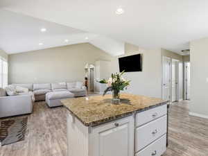 Kitchen with white cabinets, a center island, light stone countertops, arched walkways, and light wood finished floors