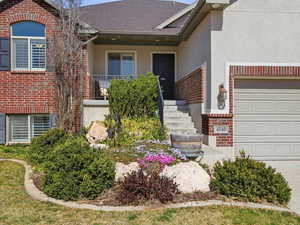 Doorway to property featuring a porch, brick siding, stucco siding, driveway, and an attached garage
