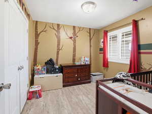 Bedroom featuring wallpapered walls, an accent wall, light wood-style flooring, a closet, and a crib