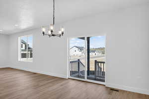 Unfurnished dining area featuring a chandelier, light wood-type flooring, and a textured ceiling