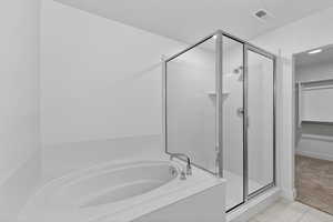 Bathroom featuring a walk in closet, a stall shower, light tile patterned floors, a garden tub, and light carpet