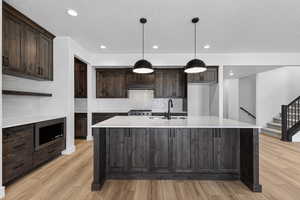 Kitchen featuring dark wood finish cabinets, light stone counters, stainless steel microwave, an island with sink, and a textured ceiling
