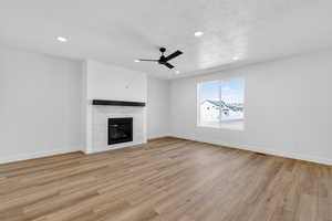Unfurnished living room with a ceiling fan, light wood-type flooring, a textured ceiling, a glass covered fireplace, and recessed lighting