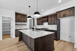 Kitchen with dark wood finish cabinets, light wood-style floors, pendant lighting, a center island with sink, and light stone countertops