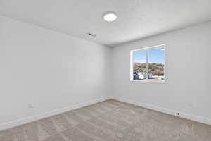 Empty room with light carpet and a textured ceiling