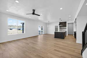 Unfurnished living room featuring hanging lights, a ceiling fan, light wood-type flooring, and a textured ceiling