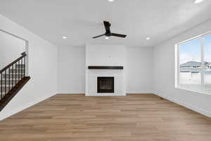 Unfurnished living room featuring a ceiling fan, light wood finished floors, recessed lighting, a tiled fireplace, and a textured ceiling
