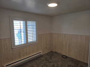 Empty room featuring a baseboard heating unit, wood walls, dark carpet, and a wainscoted wall