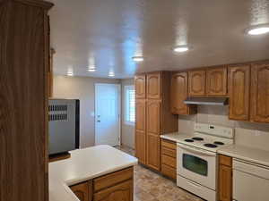 Kitchen with white appliances, wood finish cabinetry, light countertops, a textured ceiling, and stone finish flooring