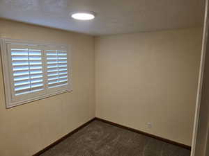Spare room with a textured ceiling, dark colored carpet, and a textured wall