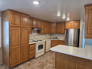 Kitchen featuring white appliances, light countertops, stone finish floors, wood finish cabinetry, and recessed lighting