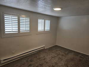 Unfurnished room with a baseboard radiator, a textured ceiling, and dark colored carpet