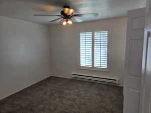 Spare room featuring a baseboard radiator, a ceiling fan, and dark carpet