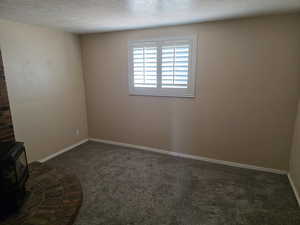 Unfurnished room featuring dark carpet, a wood stove, and a textured ceiling