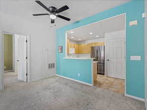Kitchen with light carpet, light wood finish cabinetry, freestanding refrigerator, light countertops, and ceiling fan