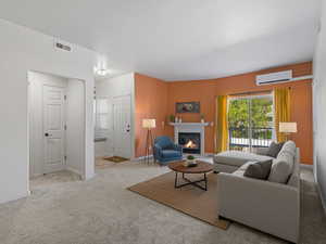 Living area with a glass covered fireplace, light carpet, and a wall mounted mini split