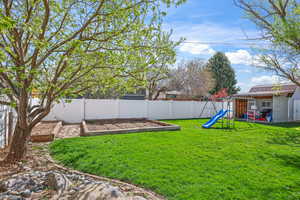 Fenced backyard featuring a playground, a garden, an outbuilding, and a patio area