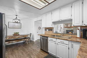 Kitchen with white cabinets, decorative backsplash, stainless steel appliances, dark wood-style floors, and a fireplace