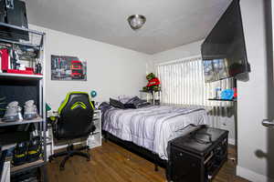 Bedroom featuring a textured ceiling, dark wood-style floors, and an office area