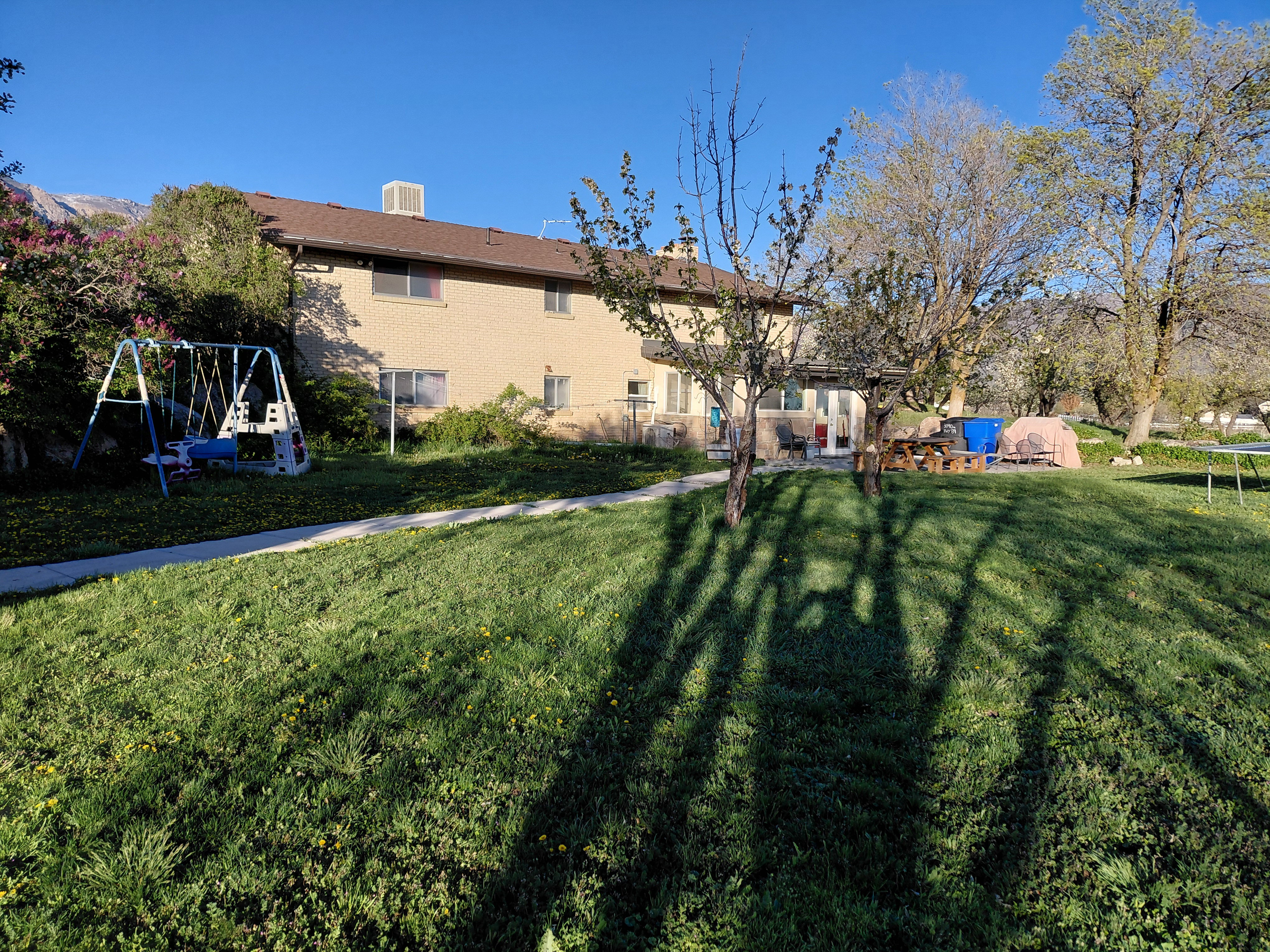 Back of property featuring a trampoline, a chimney, a yard, and brick siding