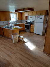 Kitchen with a peninsula, freestanding refrigerator, light countertops, stainless steel electric range oven, and light wood finished floors