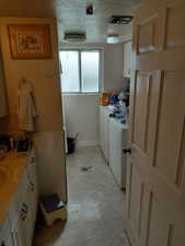 Laundry area with a textured ceiling, washer and clothes dryer, and cabinet space located in bathroom