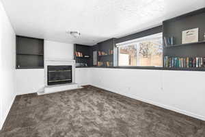 Unfurnished living room with dark colored carpet, a textured ceiling, built in features, and a glass covered fireplace
